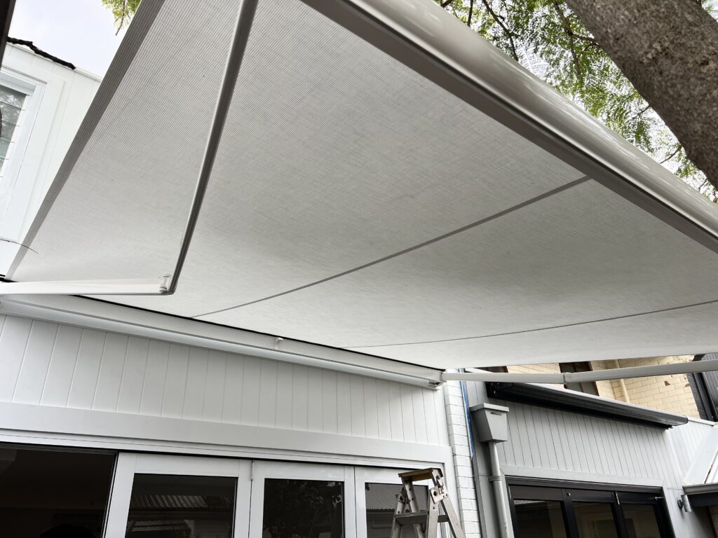 All white retractable motorised folding arm awning installed on the building facade over the courtyard in Subiaco, Perth WA